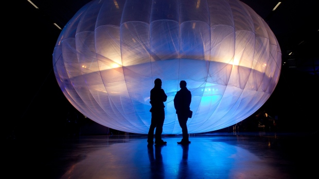 Visitors stand next to a high altitude WiFi internet hub, a Google Project Loon balloon, on display at the Airforce Museum in Christchurch on June 16, 2013.