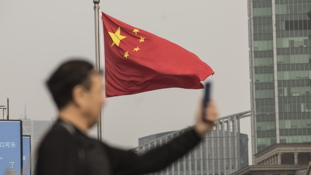 A Chinese national flag flies as a man uses a smartphone in Shanghai, China, on Tuesday, Nov. 27, 2018.