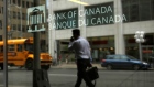 A man is reflected in a window while walking past the Bank of Canada office in Ottawa