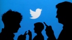 People holding phones are silhouetted against a backdrop projected with the Twitter logo