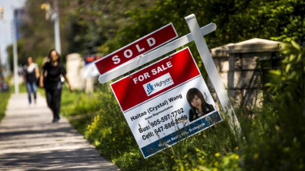 A woman walks towards a "for sale" sign of a home that has been sold in Toronto, Canada. 