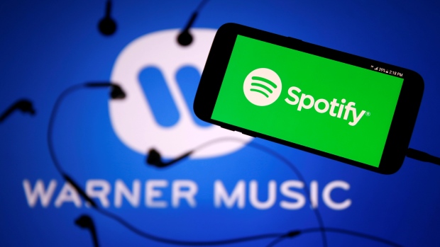 Spotify's logo is seen on a smartphone in front a Warner Music logo in this picture illustration