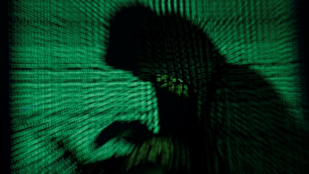 A hooded man holds a laptop computer as cyber code is projected on him in this illustration picture.