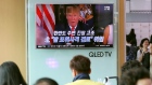 People watch a TV screen showing a local news program with an image of U.S. President Donald Trump